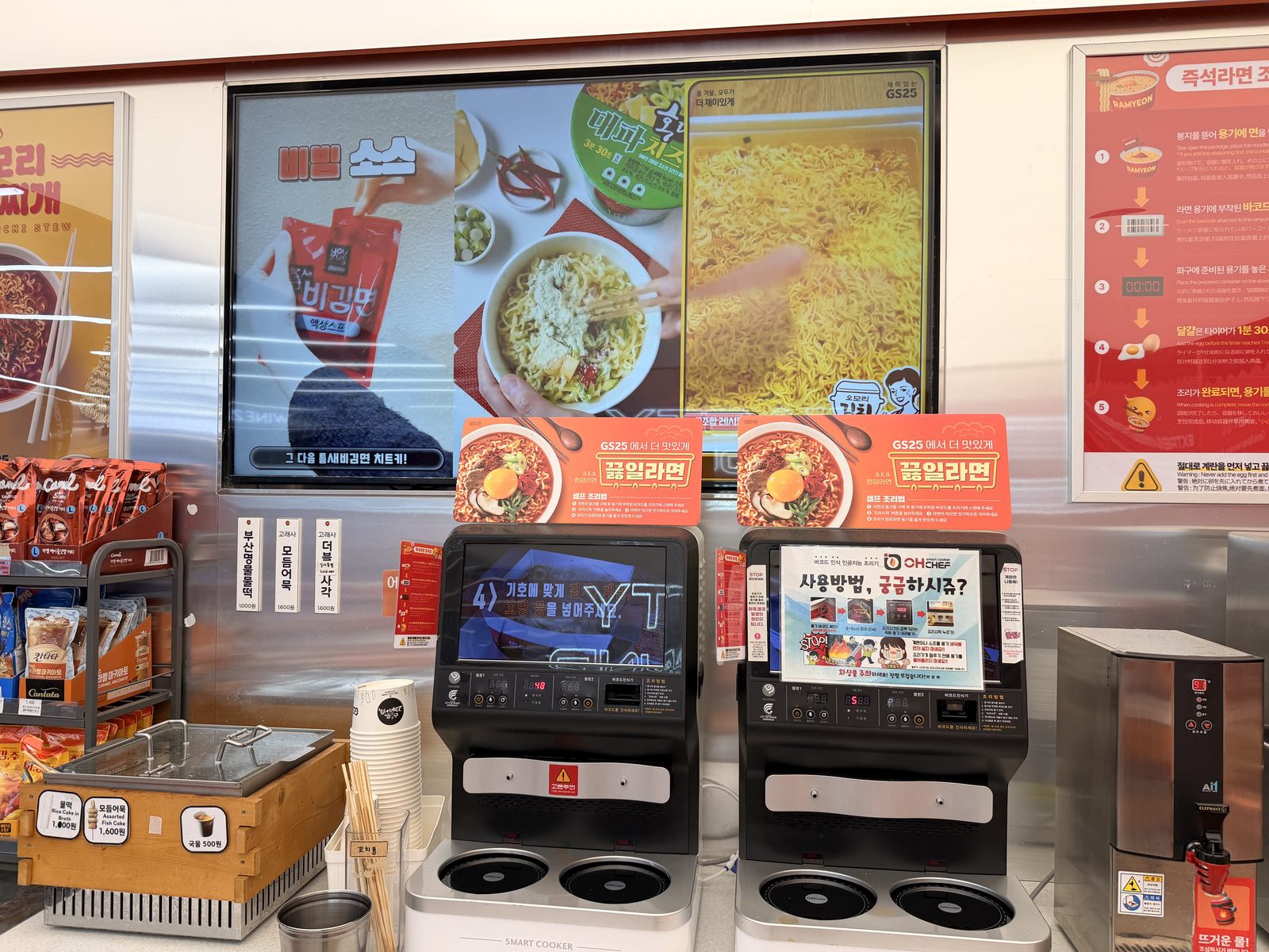 2 instant ramen cooking machines at a GS25 in Seoul, under a screen and a poster showing how to use them