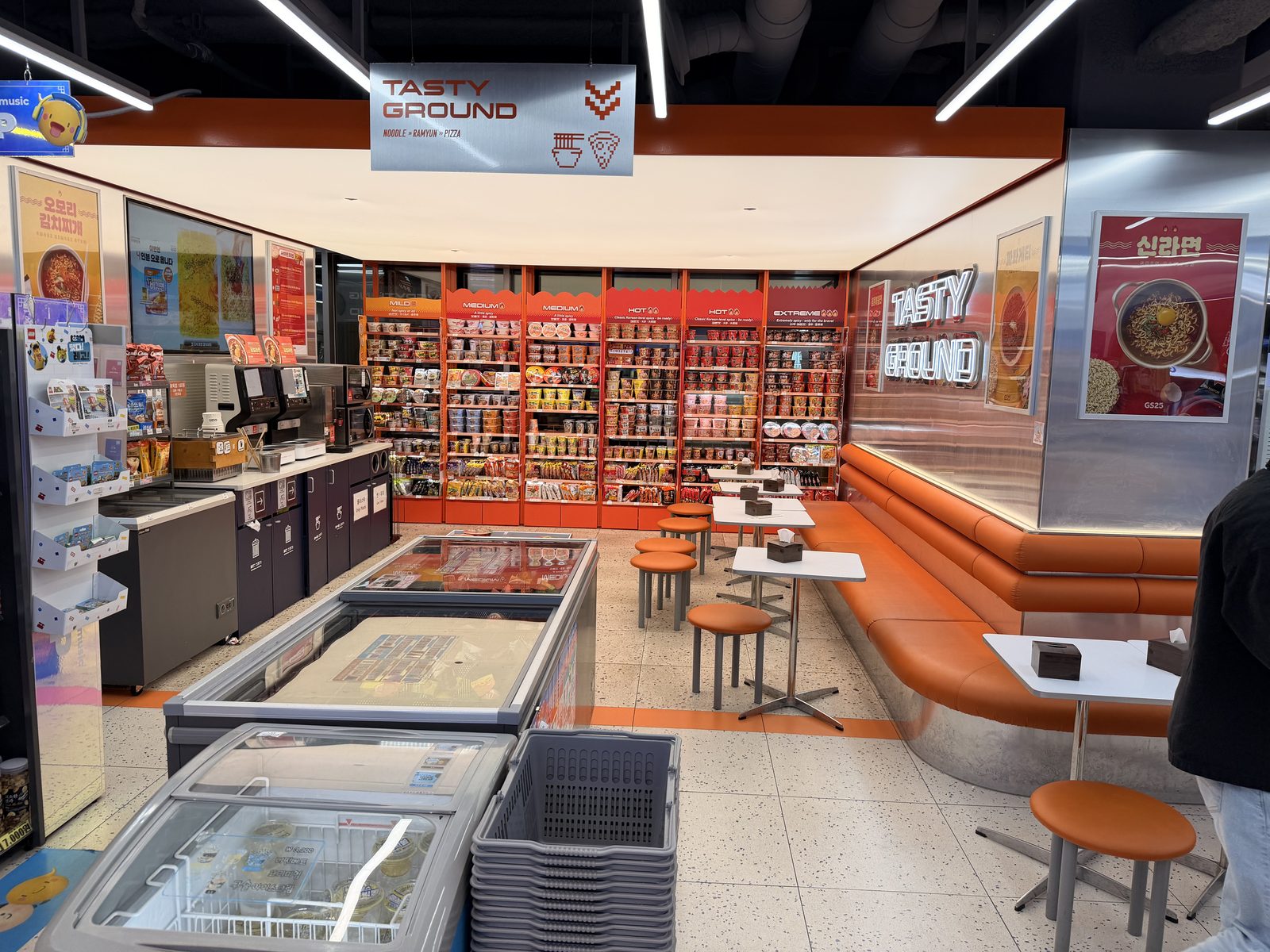 A GS25 eat-in corner in Seoul with ramen shelves sorted by spice level, cooking machines and seating