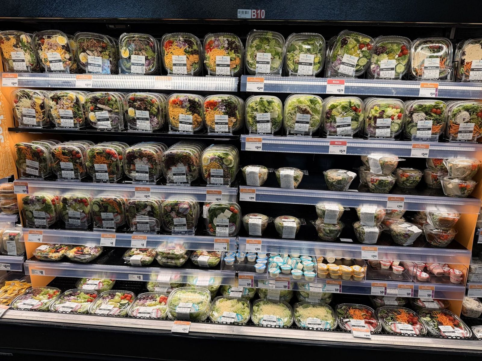 H-E-B salad wall with rows of packaged entrée salads, side salads and small dressing cups