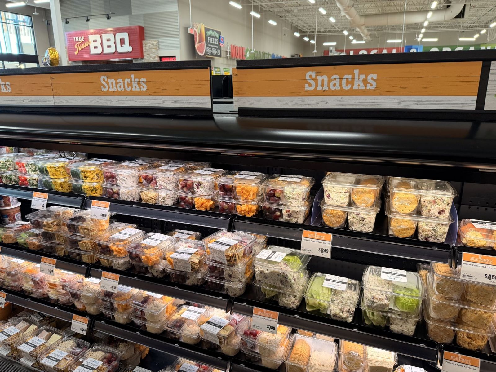 H-E-B snack trays of chicken salad, cheese, fruit and crackers under a Snacks sign