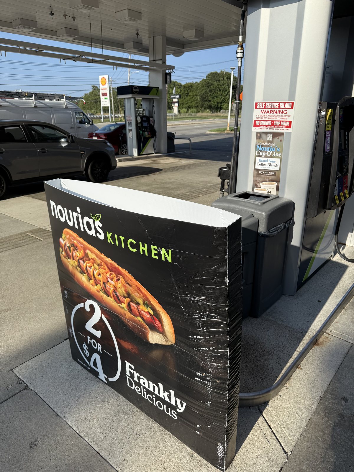 A Nouria's Kitchen sign at the pump island: 2 hot dogs for $4, Frankly Delicious