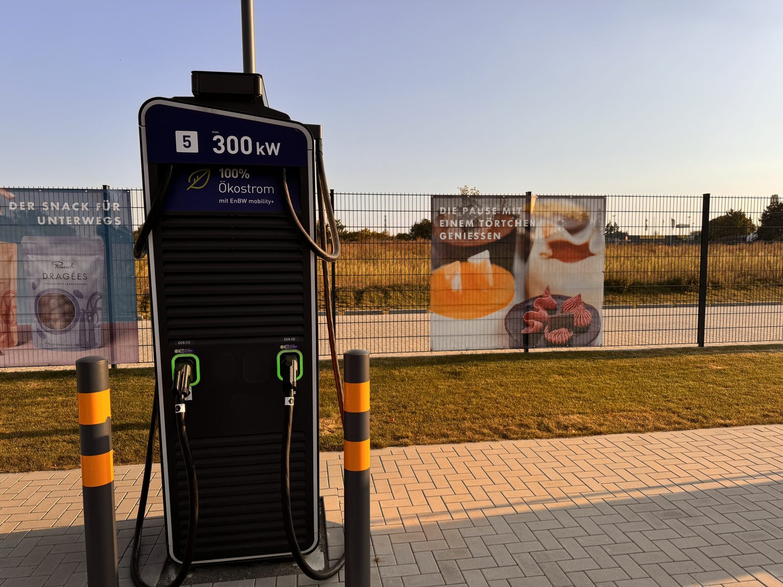 A banner on the fence beside an EnBW charger at Rausch, suggesting a break with a tartlet