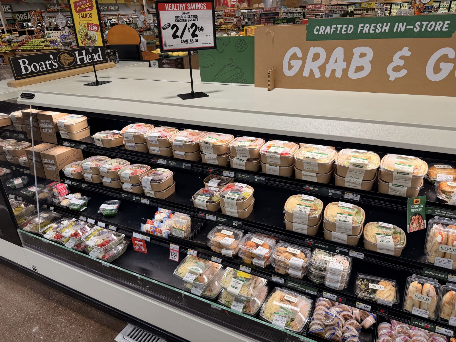Sprouts grab-and-go salad case under a sign offering diced and seared chicken breast at 2 for $2.99